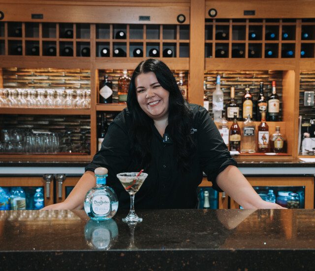 bartender standing behind bar with a martini on it