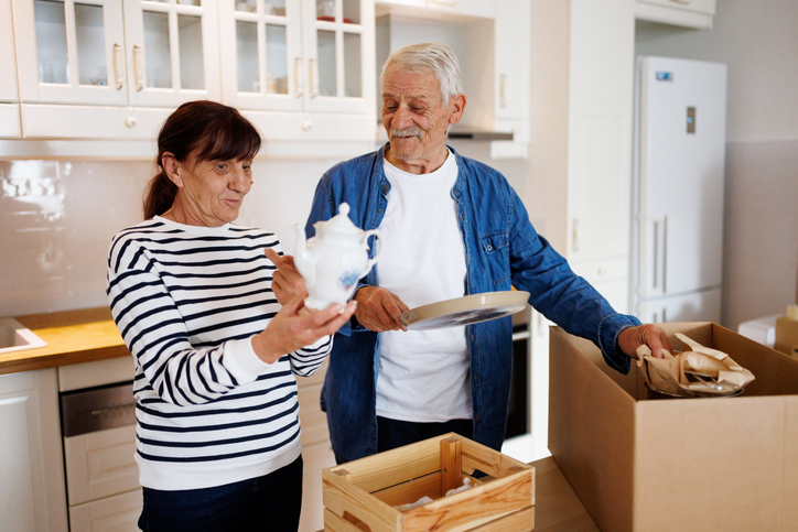 Happy senior couple unpacking a cardboard box with dishes in the kitchen during relocation