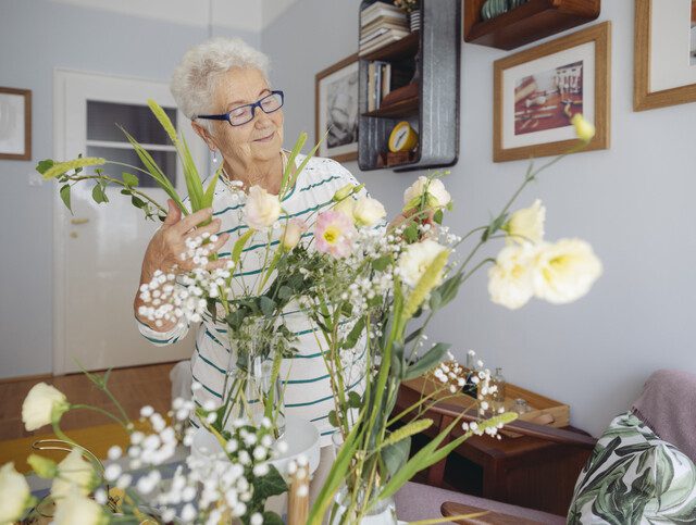 older adult woman arranging flowers in her living room