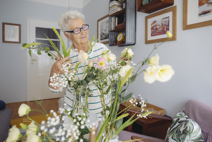 older adult woman arranging flowers in her living room